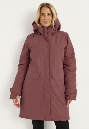 Vrouw draagt een lange, mauve geïsoleerde winterjas met capuchon, klepzakken en verstelbare manchetten tegen een effen witte achtergrond.