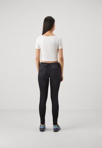 Jeans negros ajustados con un corte de cintura media, cremalleras en los bolsillos traseros y una textura suave. Combinados con una camiseta de tirantes blanca ajustada y zapatos azules.