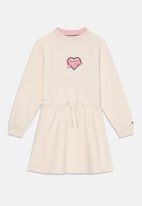 Kremowa sukienka dresowa z różowym kołnierzykiem i ściągaczem w talii. Posiada logo serca w czerwonym i niebieskim na piersi. Długie rękawy.