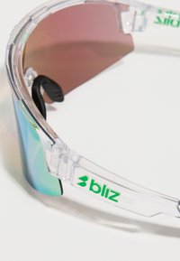 Διαφανή αθλητικά γυαλιά ηλίου με πράσινο λογότυπο και αντανακλαστικούς πολύχρωμους φακούς, εμφανιζόμενα σε κοντινή γωνία σε λευκό φόντο.