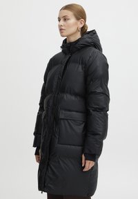 Cappotto puffo nero con cappuccio, caratterizzato da ampie sezioni trapuntate, zip frontale e due tasche laterali. Tessuto liscio e lucido con una vestibilità comoda.