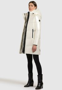 Puffer coat with a glossy white exterior, black zipper accents, and a hood. Features quilted design and side pockets. Paired with black leggings and boots.