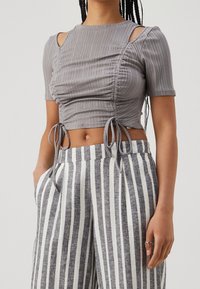 Šedý žebrovaný crop top s krátkými rukávy, vystřiženými rameny, řasenými boky a detaily na vázání, v kombinaci s proužkovanými širokými kalhotami.