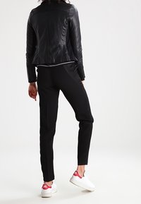 Giubbotto in pelle nera con design aderente, dettagli a coste, pantaloni neri e sneakers bianche con accenti rossi. Texture liscia in tutto.