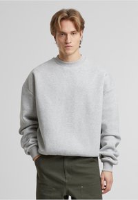 Grå sweatshirt med rund halsudskæring, drop shoulder og ribstrikkede ærmer, lavet af blødt materiale. Bæres med olivengrønne bukser.
