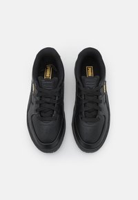 Svarta sportskor med en slät läderöverdel, rund tå, vadderad krage och platta snören, med en guldig logotyp på tungan.