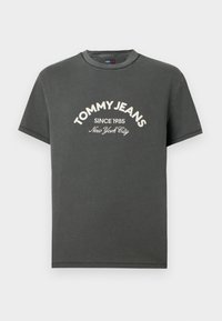 Γκρι βαμβακερό t-shirt με κοντά μανίκια, στρογγυλή λαιμόκοψη και λευκό κεντημένο κείμενο: "TOMMY JEANS SINCE 1985 Νέα Υόρκη" στο μπροστινό μέρος.