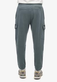 Spodnie cargo w stonowanej zieleni w kolorze teal, z kieszeniami bocznymi, zwężanym krojem, ściągaczami na nogawkach oraz gładkim materiałem z mieszanki bawełny.
