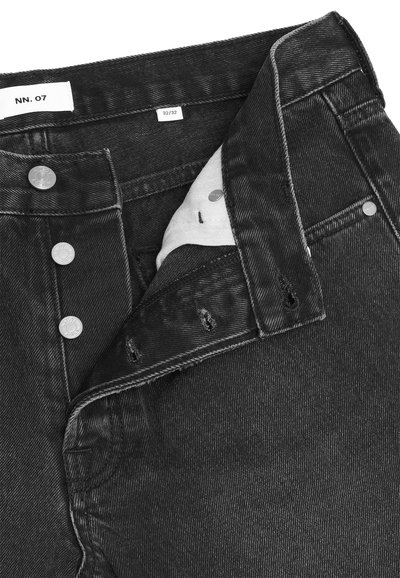 Mustat denimfarkut, joiden nappivetoketju on osittain auki, paljastaen valkoisen vuorin ja koon 32/32 vyötärökaitaleen sisäpuolella.