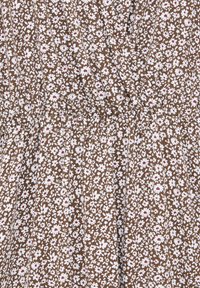 Tissu marron avec un motif dense de petites fleurs blanches aux centres rouges, avec une couture élastique froncée pour un détail ajusté.