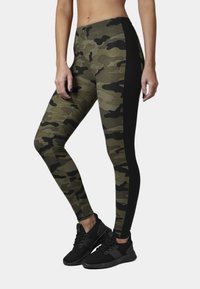 Camouflage leggings with a black side panel, featuring a fitted design and stretchy fabric, paired with black athletic shoes.