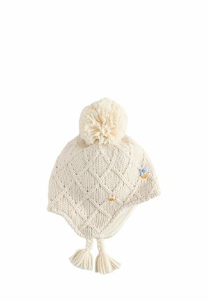 Căciulă tricotată bej cu un model în diamant, având un pom-pom pufos în vârf și flori decorative. Include ciucuri pe laterale.