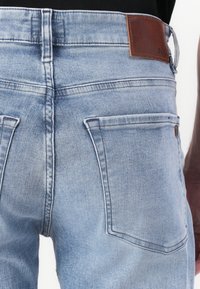 Vaqueros de denim azul claro con corte ajustado, que cuentan con dos bolsillos traseros, una cintura cosida y una etiqueta de logo de piel marrón.