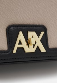 Czarna i beżowa torebka strukturalna z fakturowaną powierzchnią, złotym okuciem i wytłoczonym logo z kątowym wzorem.