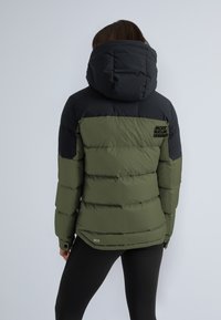 Veste rembourrée à col, sections vertes et noires, texture matelassée, logo brodé au dos, manches ajustées, bas avec détail accentué.