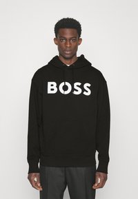 Felpa nera in cotone con tasca a marsupio, cappuccio con cordino e grande logo bianco "BOSS" sul davanti. Vestibilità regolare con polsini a coste.