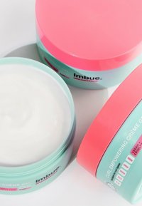 Mintgroene en roze potten met krulcrème waarin het witte product zichtbaar is. Labels geven aan dat het veganistisch en diervriendelijk is. Gladde, glanzende afwerking.