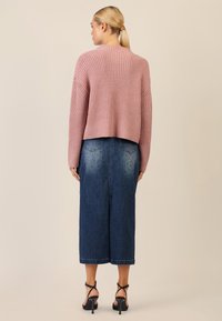 Pink ribbed knit sweater with a cropped design, paired with a knee-length denim skirt featuring a scattered stud pattern and pockets.