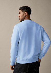 Lichtblauwe sweatshirt met ronde hals van stof met een gladde textuur, met ribgebreide manchetten en zoom, gedragen met donkere jeans.