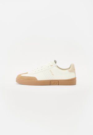 Zapatillas blancas con detalles de ante color marrón, puntera redondeada, paneles laterales perforados, diseño con cordones y suela de goma con una etiqueta de la marca.