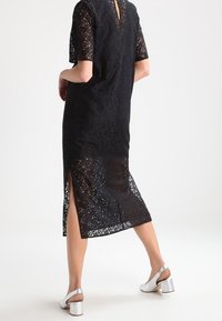 Svart spetsklänning med korta ärmar, V-ringning, sidofickor och ett texturerat mönster. Matchad med silverfärgade klacksandaler.