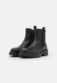 Mustad musta nahast põlvesaapad elastsete külgpaneelidega, ümar toe ja massiivne kummist talla, millel on tekstuuriga profiil. Lihtsaks selga panemiseks tõmbetab.