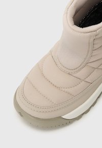 Bottine matelassée beige clair avec un bout arrondi et un upper doux et rembourré, dotée d'une semelle en caoutchouc épaisse pour une meilleure adhérence.