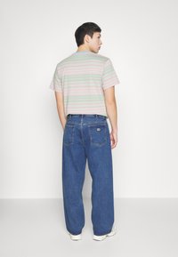 Camiseta de manga corta a rayas en colores pasteles, combinada con unos vaqueros de denim azul de corte holgado que cuentan con un parche en la parte trasera y dos bolsillos traseros.