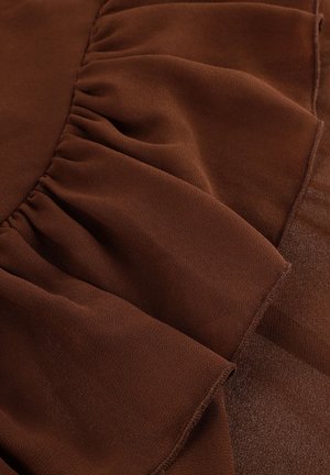 Bruine stof met gather- en rimpeldetails en een gladde textuur, waarop gestikte naden en gelaagde plooien zichtbaar zijn.