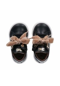 Scarpe di pelle nera con una texture liscia, caratterizzate da un fiocco in velluto beige, lacci elastici, occhielli dorati e suole in gomma bianca.
