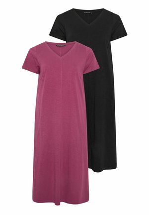 Vrouw met lang bruin haar, gekleed in een paarse jurk met korte mouwen, V-hals en enkel-lengte, en bruine sandalen, staand tegen een neutrale muur.