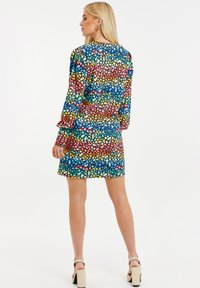 Värikäs pilkullinen mekko, jossa on pitkät hihat, pyöreä kaula-aukko ja virtaava muotoilu. Kankaan pinta on sileä, ja siinä on kirkas kuvio.