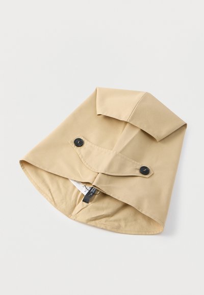 Μπεζ καπέλο βροχής με φαρδιά γείσο, κατασκευασμένο από λείο αδιάβροχο υλικό. Διαθέτει αναδιπλούμενο πάνω μέρος και δύο μαύρα διακοσμητικά κουμπιά.