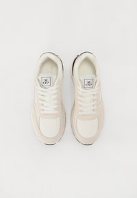 Lys beige sneakers med hvit mesh og semsket overlegg, rund tå, flate lisser og svarte såler. Logoetikett på tungen.