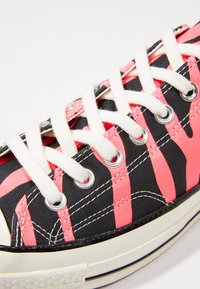 Canvas sneakers med ett svart och rosa randigt mönster, vita snören och metallöglor. Vit gummisula med en texturerad yta.