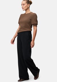 Haut marron à carreaux, à manches courtes et épaules ballons, associé à un pantalon large noir et des chaussures noires à motif en maille.