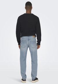 Black ribbed sweater, light blue jeans with back pockets, and black sneakers. Sweater has long sleeves, jeans feature a relaxed fit.