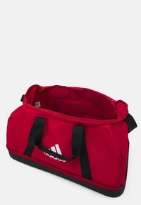 Rode sporttas met zwarte accenten, gemaakt van duurzaam materiaal, heeft een grote binnenruimte en contrasterende zwarte banden. Adidas-logo prominent weergegeven.