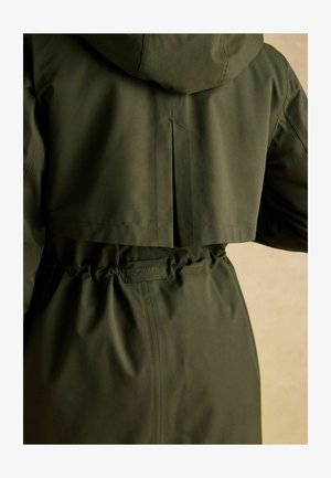 Grüne Kapuzenjacke mit tailliertem Bund, strukturierter Stoff und Rückenfalten-Detail. Mit sichtbarem Joules-Label an der Taille.