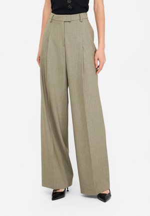 Pantaloni a gamba larga in tessuto grigio chiaro, con vita alta, pieghe e design su misura, abbinati a scarpe nere a punta.