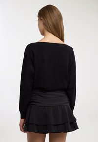 Maglione nero in maglia con scollo ampio e maniche lunghe, abbinato a una minigonna nera a strati con balze, realizzata in tessuto leggero.