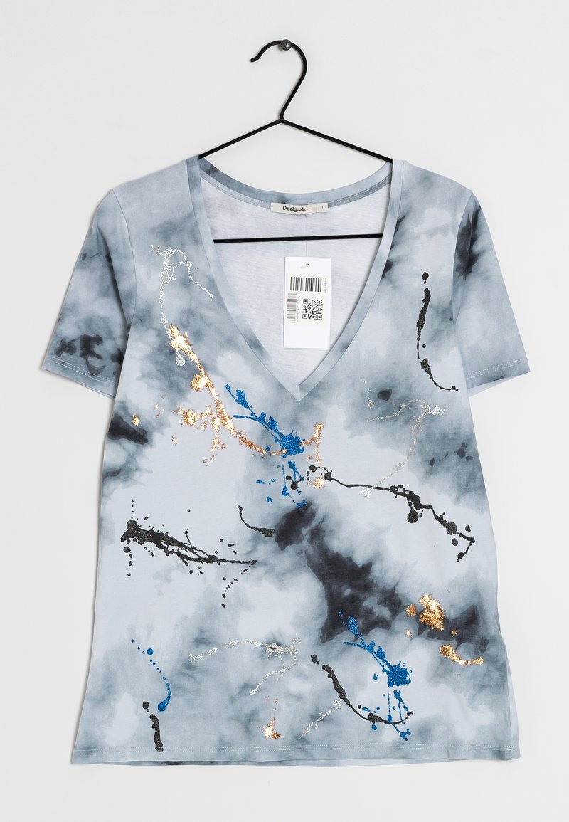 T-shirt bleu clair à col en V avec un design de taches de peinture abstraites noires, bleu, argent et or, accroché à un cintre noir avec une étiquette de prix.