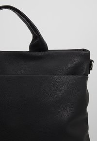 Černá texturovaná taška s hladkým povrchem, vybavená pevným držadlem a diskrétním švem podél okraje.