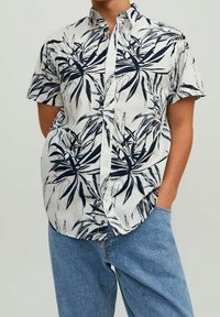 Camicia a maniche corte con bottoni, base bianca con motivo di foglie blu scuro. Tessuto morbido, vestibilità regolare, design casual e colletto.