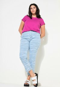 Fuchsiové tričko s krátkým rukávem, světle modré džíny se zebrovaným potiskem a bílé sandály s černými podrážkami. Jednoduchý design a volný střih.