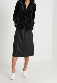 Czarna aksamitna koszula z guzikami i kieszonką, zestawiona z czarną skórzaną spódnicą midi; uzupełniona białymi mule'ami z odkrytymi tyłami. Prosty i stonowany design.