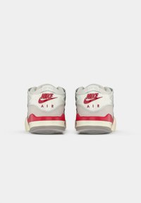 Nike Air sportbačiai su pilku ir baltu viršumi, raudonomis detalėmis ir senoviniu grietinėlės spalvos padu; galinis vaizdas rodo logotipą ant kulno.