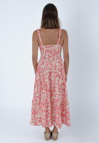 Abito maxi floreale rosa con spalline arricciate e design a strati. Presenta un corpetto aderente e una gonna fluida, realizzato in tessuto leggero.