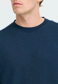 Sudadera de cuello redondo en azul marino, hecha de un suave tejido texturizado. Presenta un escote acanalado y una superficie lisa, sin patrones ni adornos.