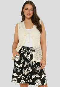 Krämfärgad, stickad väst med spetsmönster och knut framtill. I kombination med svarta shorts med vit blommönster och knytband i midjan.